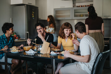 A group of friends shares a laugh while having a casual meal in a modern kitchen setting. The...