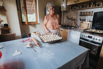 An elderly woman stands in a cozy kitchen, preparing fresh homemade pastries. The scene captures the warmth of traditional home baking and the joy of creating delicious treats.