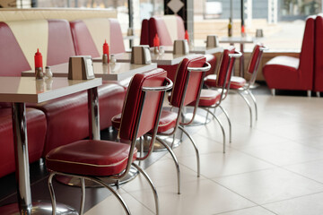 Red leather seats and silver accents in classic 1950s diner creating nostalgic atmosphere with empty tables and condiment dispensers adding to retro style
