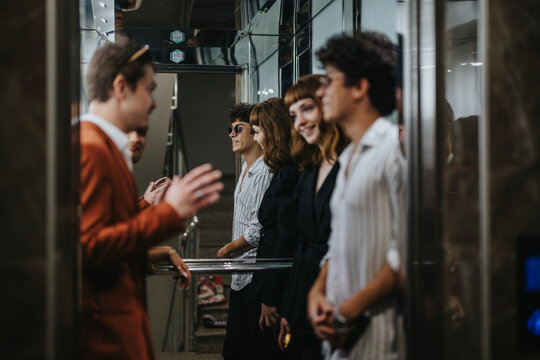 A group of young professionals engage in a lively conversation inside a sleek, modern elevator. They appear relaxed and friendly, enhancing the sense of a positive social interaction.