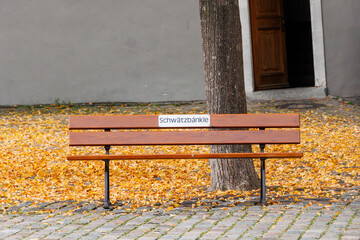 A bench in yellow autumn leaves with a text in German, Swabian dialect Schwätzbänkle which means...