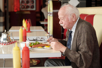 Senior man eating meal in classic diner featuring retro decor and vibrant colors. Man enjoying fresh meal while seated at table with various condiments surrounding him