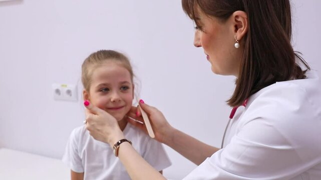 Female doctor examining little girl mouth at office. Doctor at hospital checking the sore throat of kid patient. Pediatrician checking tonsils of little patient in hospital room, white background