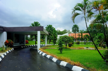 A serene villa surrounded by lush greenery, featuring a traditional yet modern architectural design with a sloping red-tiled roof. The villa is nestled amidst a garden landscape