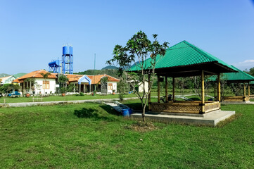 A serene villa surrounded by lush greenery, featuring a traditional yet modern architectural design with a sloping red-tiled roof. The villa is nestled amidst a garden landscape