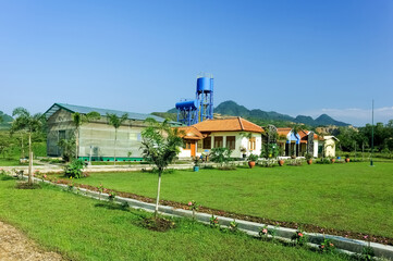 A serene villa surrounded by lush greenery, featuring a traditional yet modern architectural design with a sloping red-tiled roof. The villa is nestled amidst a garden landscape