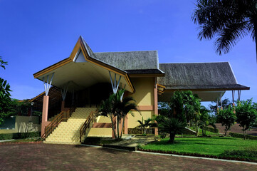 A serene villa surrounded by lush greenery, featuring a traditional yet modern architectural design with a sloping red-tiled roof. The villa is nestled amidst a garden landscape