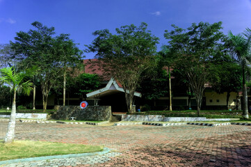 A serene villa surrounded by lush greenery, featuring a traditional yet modern architectural design with a sloping red-tiled roof. The villa is nestled amidst a garden landscape