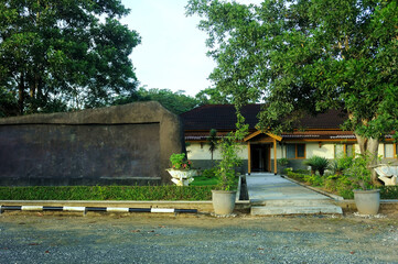 A serene villa surrounded by lush greenery, featuring a traditional yet modern architectural design with a sloping red-tiled roof. The villa is nestled amidst a garden landscape