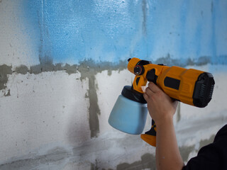 girl paints concrete wall blue with spray gun