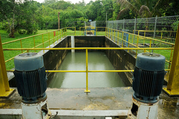 A Water Treatment with a walkway bridge leading to a series of large, circular water treatment tanks at an industrial facility. The yellow handrails on either side of the blue metallic walkway provide