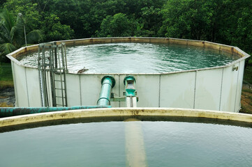 Water treatment octagonal water storage tank at an industrial facility, with clear water filling it to the brim. A green pipeline system is attached to the tank, likely used for transferring water int