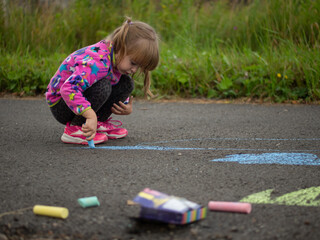girl draws with colored chalk on the asphalt