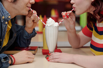 Two people enjoying a milkshake together, each sipping through striped straws while sitting closely...