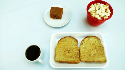 Breakfast table countaining toasts, pop corn, banana sweet and cup of coffee.