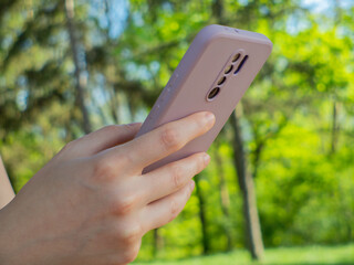 Unrecognizable woman holding her phone and scrolling social media apps and doing business while relaxing in the nature park at daytime