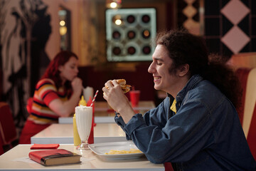 Man eating at retro-styled diner with another person in background, both enjoying their food and drinks surrounded by vintage decor