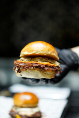 The chef wearing black gloves is holding a smashed burger.