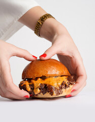 A woman with red nail polish is holding a delicious smashed cheeseburger against a white background