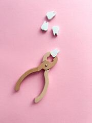 White wooden teeth and forceps on a pink background. Dental health concept. Dentist day concept. Top view, space for copy text