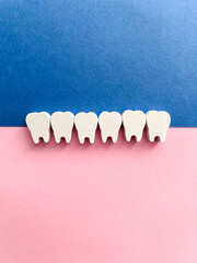 White wooden teeth on a pink and blue background. Dental health concept. Dentist day concept. Top view, space for copy text