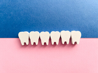 White wooden teeth on a pink and blue background. Dental health concept. Dentist day concept. Top view, space for copy text.