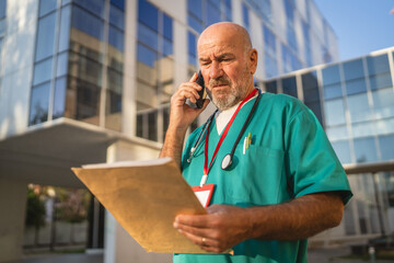Mature man doctor talk on cellphone read information from documents