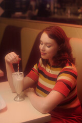 Woman relishing milkshake while sitting in cozy retro diner with striped wall design creating warm and nostalgic atmosphere