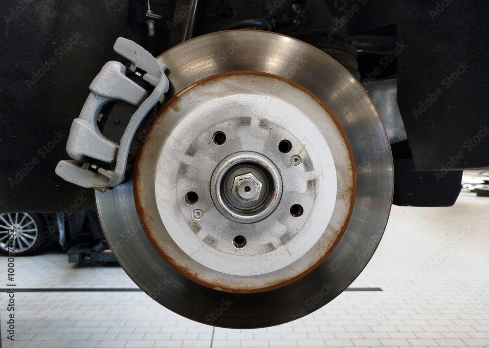 Wall mural a brake disc and brake caliper installed on a car that is on a lift in a car service center.