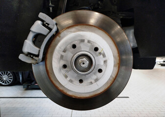 A brake disc and brake caliper installed on a car that is on a lift in a car service center.