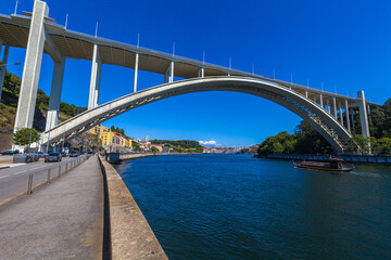 A striking architectural scene featuring a large, modern concrete arch bridge spanning across a wide river unde