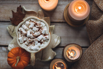 Flat lay top view. Spicy sweet fall hot drink: delicious pumpkin latte with cinnamon, marshmallow. Served in handmade artisan mug in shape of pumpkins, cozy home decor with candles, dry autumn leaves