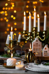 Beautiful table setting for family Christmas dinner at home. Cozy atmosphere, candlelight. Wine glasses, vintage chandelier, elegant interior. Fir tree branches, wooden furniture, dark, bokeh