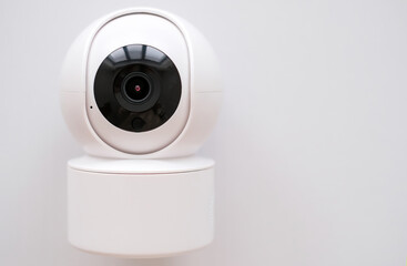 A white security camera with a black lens is mounted on a white surface. The camera is designed to capture images and record video footage