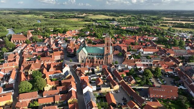 Aerial orbit shot of the majestic Ribe Cathedral against the backdrop of the historic town of Ribe, with red-tiled roofs of houses and half-timbered buildings.