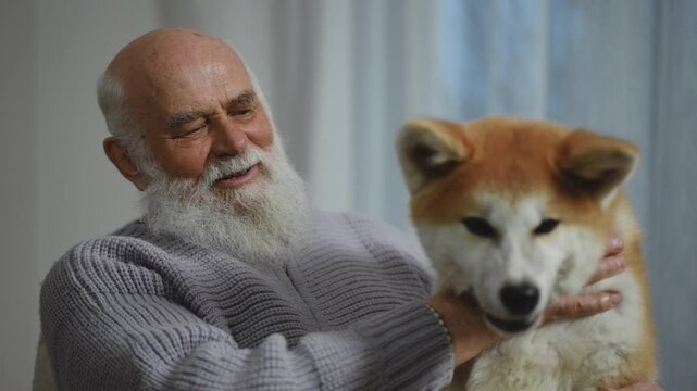 An incredibly joyful elderly man is holding his beloved dog, capturing the essence of warmth and companionship at home