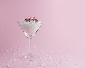 Snow with gift box in martini glass on pastel pink background. Minimal Christmas or New Year concept.