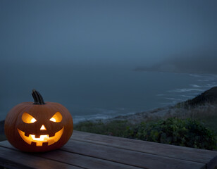 One spooky halloween pumpkin, Jack O Lantern, with an evil face and eyes on a wooden bench, table with a misty gray coastal night background