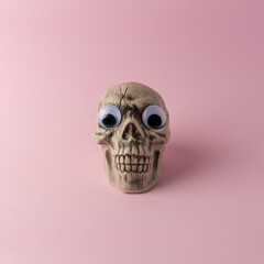 Halloween skull head with funny eyes on pink background. Funny minimal concept.