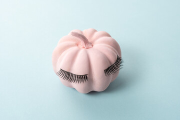 Pink Halloween pumpkin with lashes on blue background. Minimal holiday girl concept.