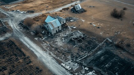 Fototapeta premium A striking aerial image of an abandoned farmhouse surrounded by barren fields and debris. The stark emptiness of the landscape, combined with dilapidated structures, reflects the passage of time and
