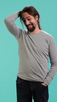Vertical video Portrait of shy man putting hand on head, feeling ashamed, isolated over studio shot. Self conscious person feeling insecure while seeing crush, feeling need to express emotions, camera