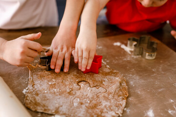 Close-up of children's hands cutting cookies with a cookie cutter on gingerbread dough
