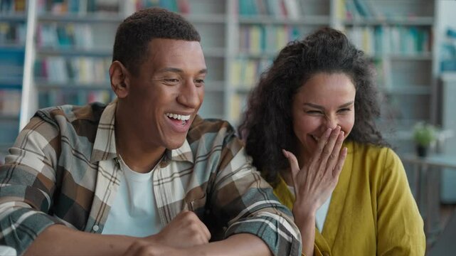 Two people African American man Indian Arabian woman team joy victory win students session diploma exam together classmates achievement laptop screen give five girl guy library good grade university