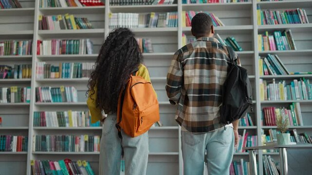 Back view man woman students library bookshelf books female male two people high school readers teens university learning knowledge study bookstore classmates friends learners college textbooks pupils