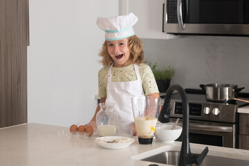 Kid chef cook cookery at kitchen. Cute boy cooking in kitchen at home kitchen. Healthy ingredients. Portrait of little child in uniform of cook. Cute child to be a chef.