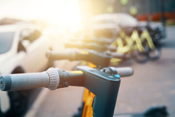 A row of electric scooters with automotive tires and electrical wiring are parked on the side of the road, featuring bicycle handlebars and automotive lighting