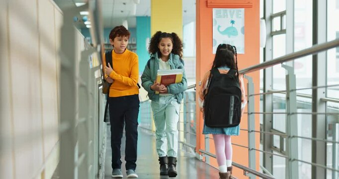 Happy, children and talking with walking, together and backpack for extracurricular at academy. Students, books and smile for education, development and scholarship in learning, friendship and school