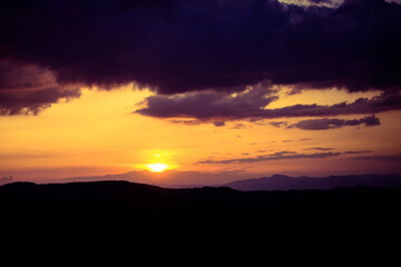 Sunset view from Campos do Jordão with dramatic dark clouds and a glowing orange sky. The silhouettes of mountains add depth to the serene