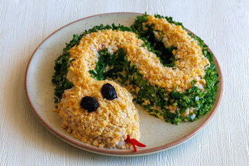 Salad with shrimps, egg, chicken, cheese and parsley in shape of green Snake as symbol of Chinese new year on a plate on a white table. Creative design for party.